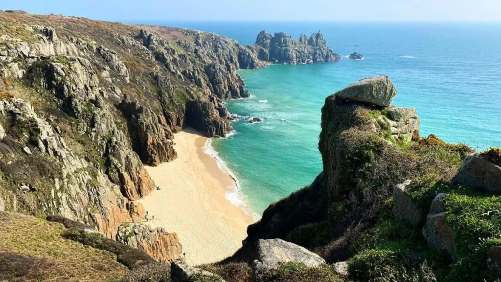 Pedn Vounder beach near Porthcurno, with golden sand reaching into turquoise water and Logan Rock rising in the distance.
