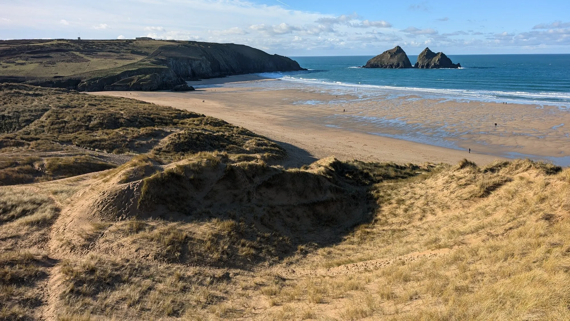 The wide sandy sweep of Holywell Bay on the north Cornwall coast, backed by dunes with the twin Gull Rocks standing offshore, a beach used as a filming location for the Poldark television series.