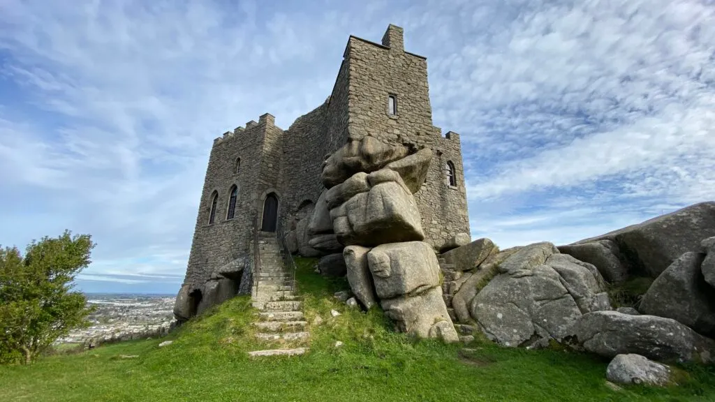 Carn Brea Castle, a small fortified granite building with crenellations, perched on rocky outcrops on the hilltop above Redruth, Cornwall.