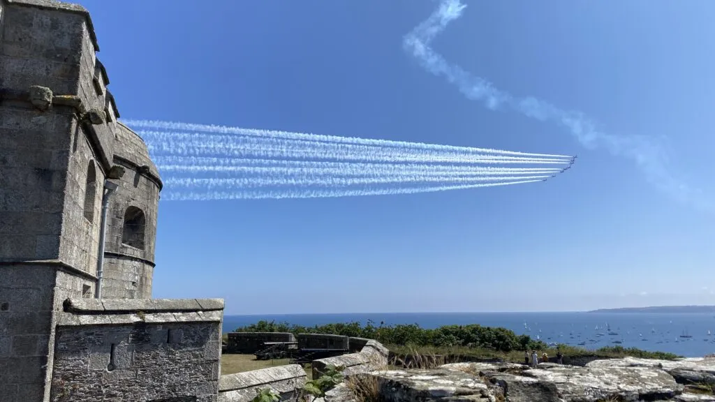 The Red Arrows displaying over Falmouth Bay during Falmouth Week, viewed from the granite ramparts of Pendennis Castle, with sailing boats anchored in the bay below.