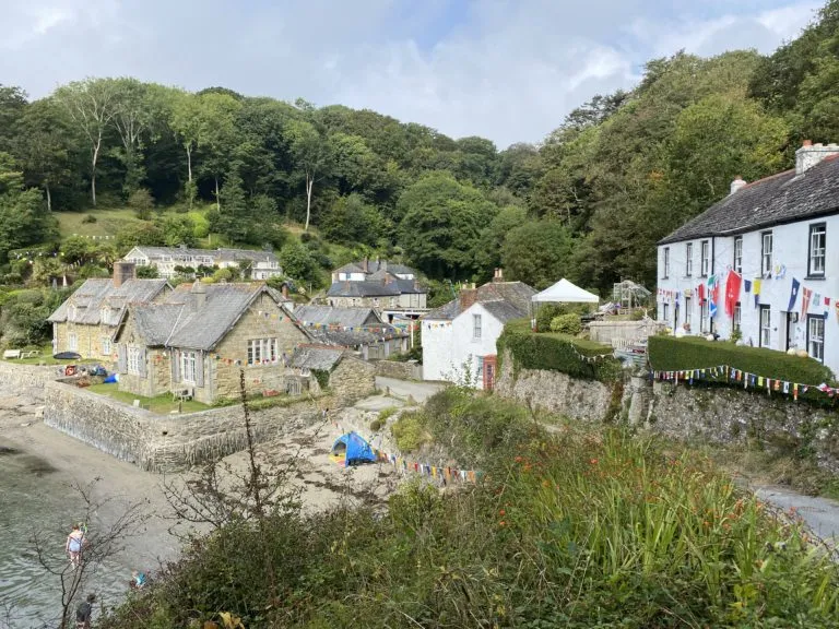 Durgan, the small National Trust hamlet on the Helford River, viewed from above with granite fishermen's cottages, the small beach, bunting and a wooded valley behind.