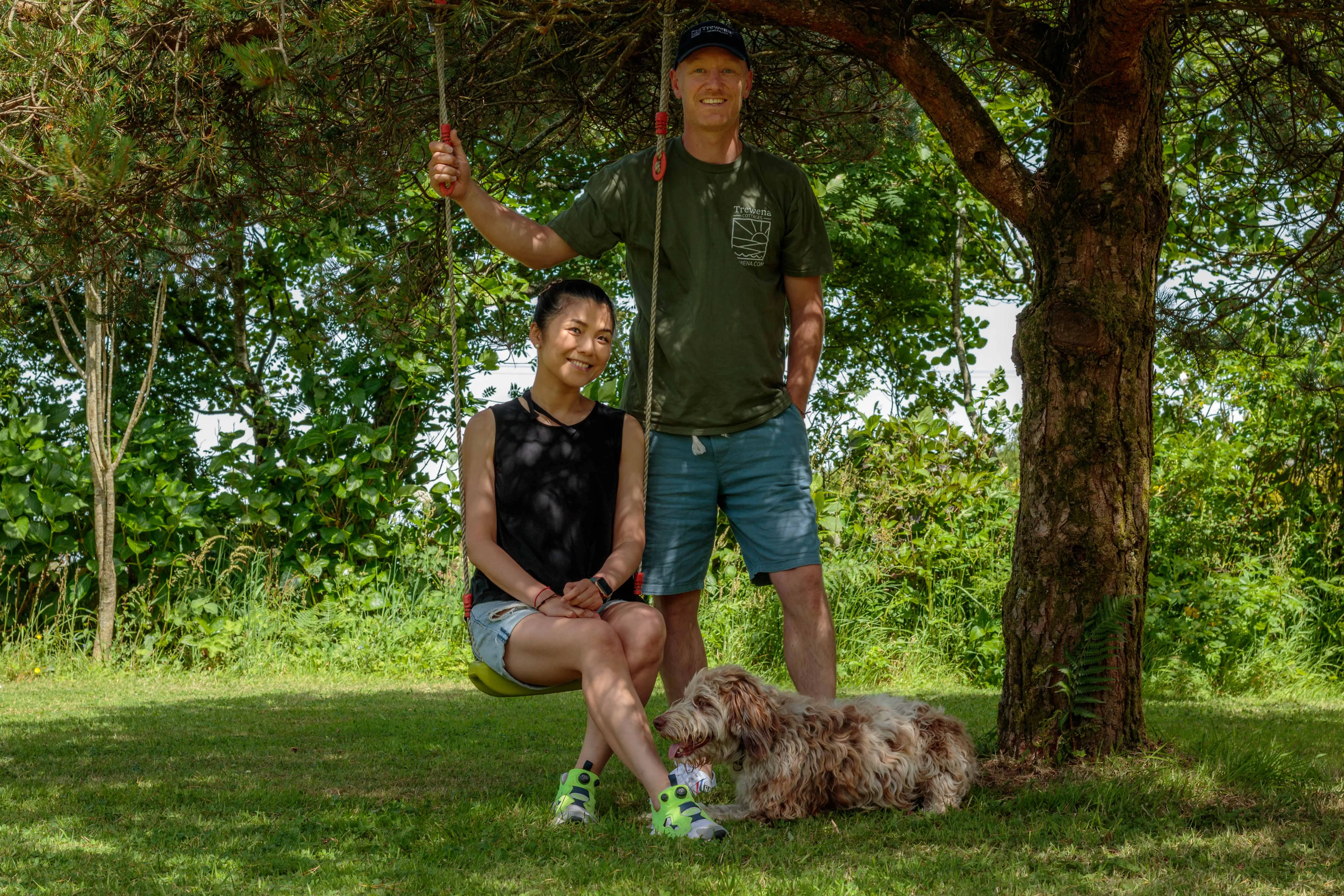 Hellen on a tree swing with Rich standing beside her in the dappled light at Trewena.