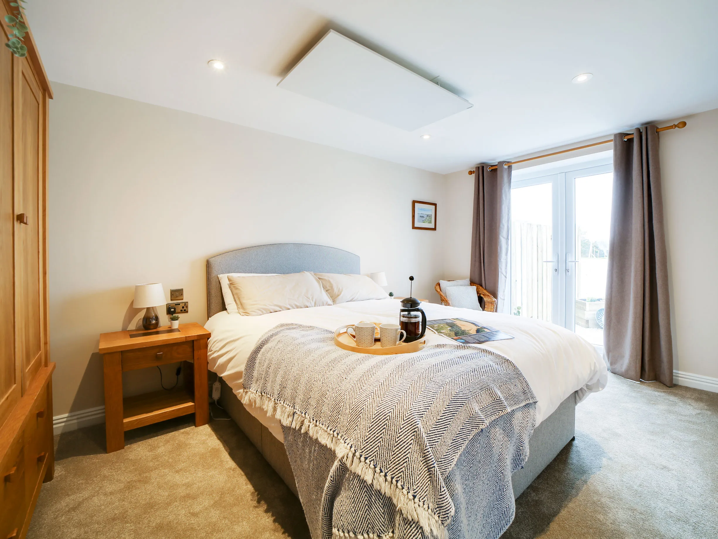A king-size bed with a breakfast tray and cafetiere, soft morning light through the French doors at The Tractor Shed.