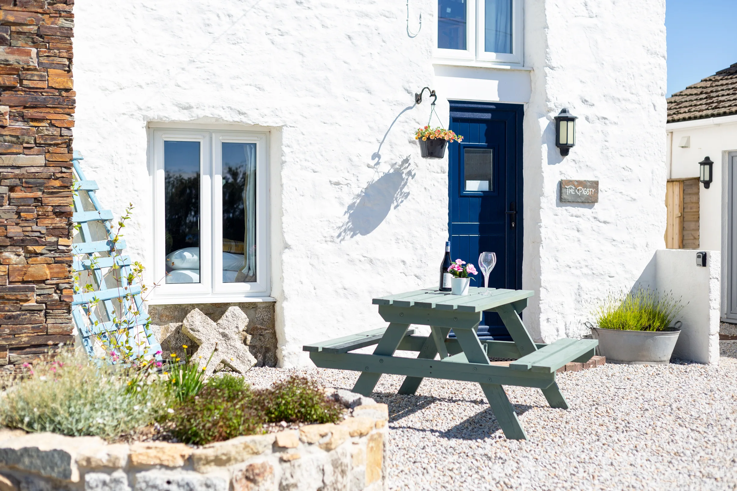 The Pigsty exterior. Whitewashed wall, blue door, picnic bench on a flagstone patio.