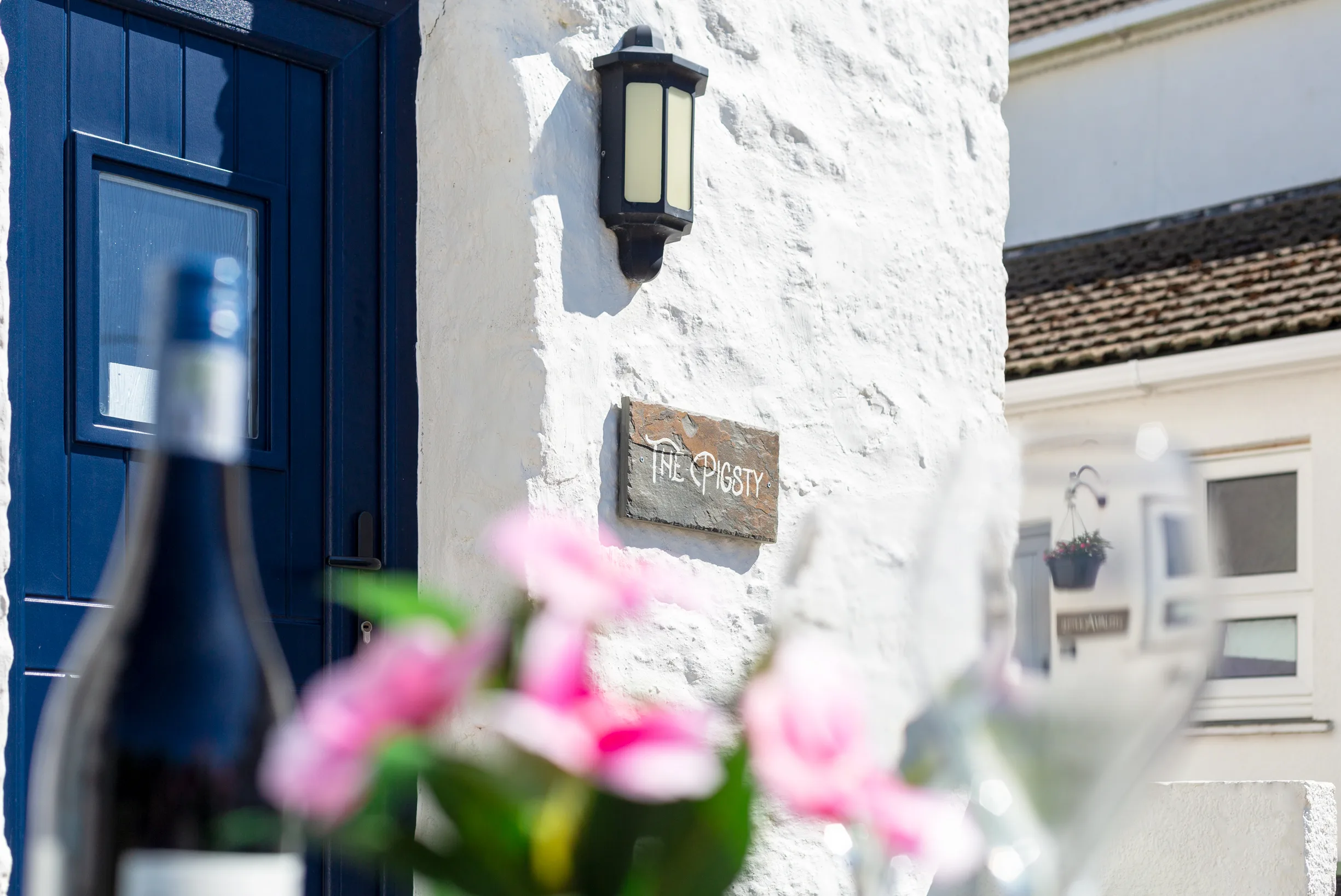The Pigsty's blue front door with slate name plate, garden in the foreground.