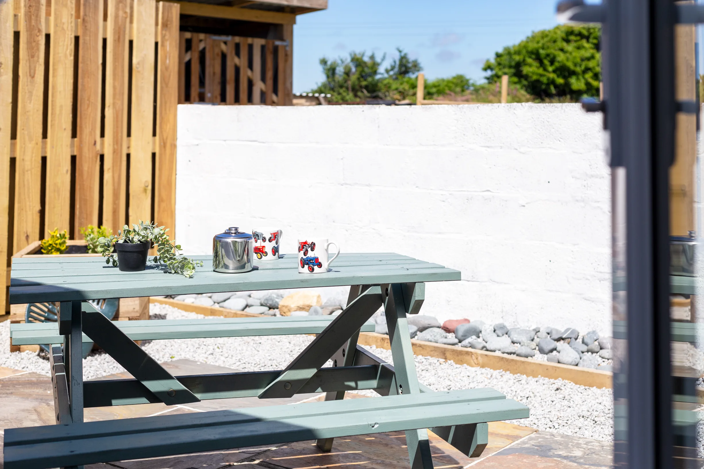 Tractor Shed patio. Sage green picnic table on gravel, white walls.