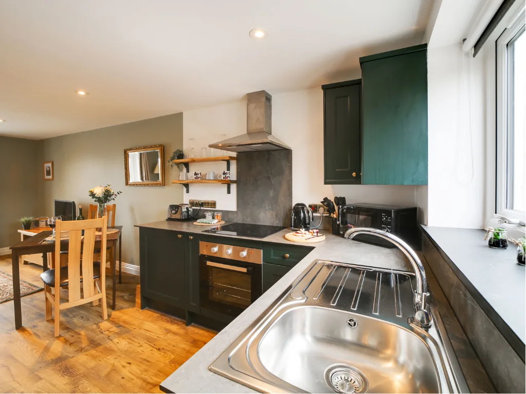 Tractor Shed kitchen. Dark green cabinets, wooden floor, dining nook by the window.
