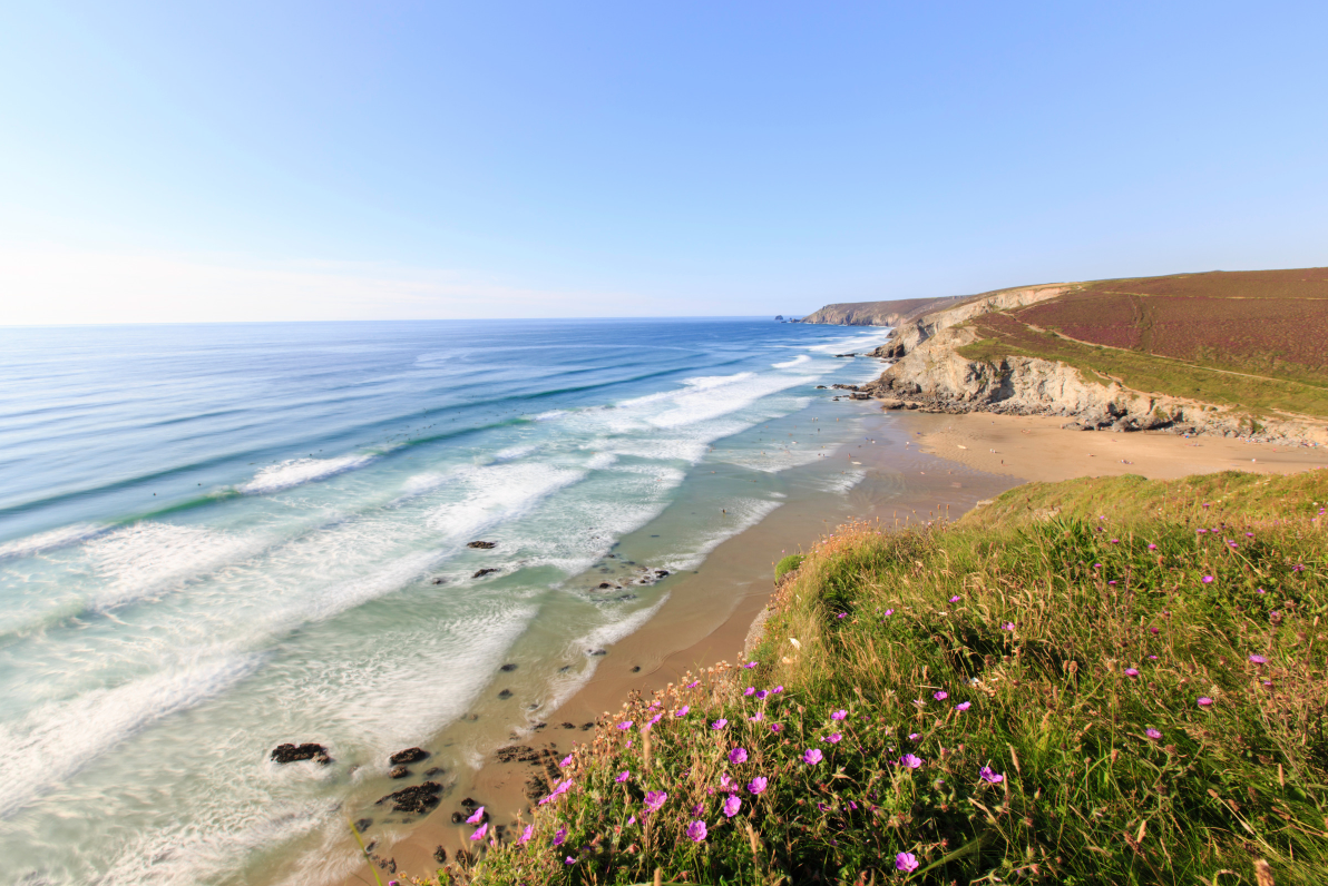 Porthtowan Beach Cornwall seen from the coast path above, cliffs on both sides framing a wide sandy beach.