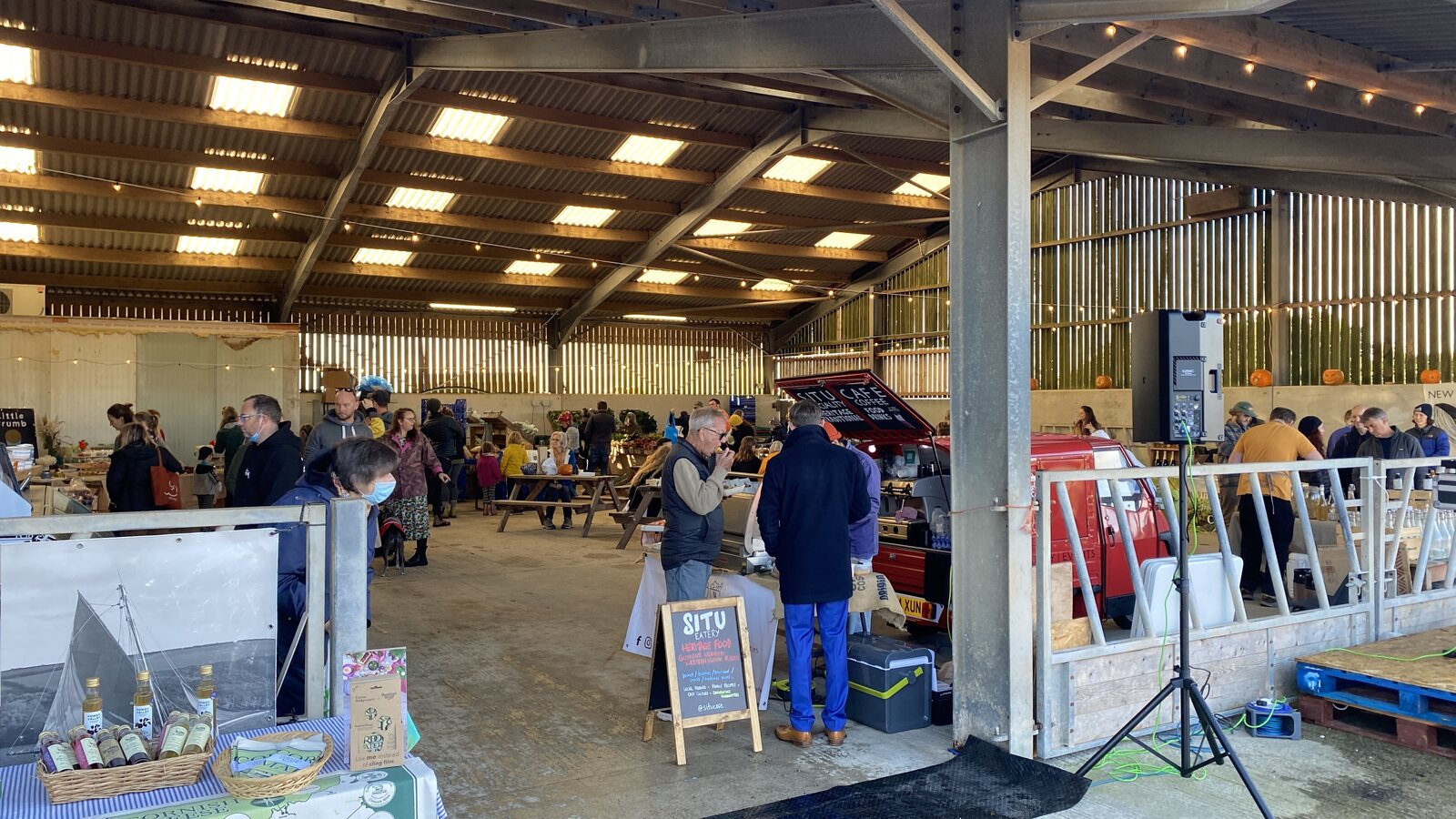 The Food Barn at Tregew, with several local producer stalls inside a large open barn selling vegetables, meats, and cheeses, customers browsing.