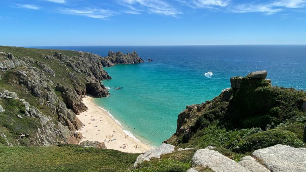 A breathtaking view of Pedn Vounder Beach, with golden sands, turquoise waters, and towering cliffs along Cornwall's rugged coastline.