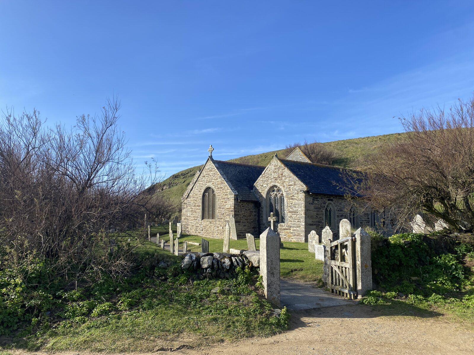St Winwaloe Church at Gunwalloe Church Cove, a medieval stone church on the dunes above a sandy beach, with the detached bell tower visible to one side.