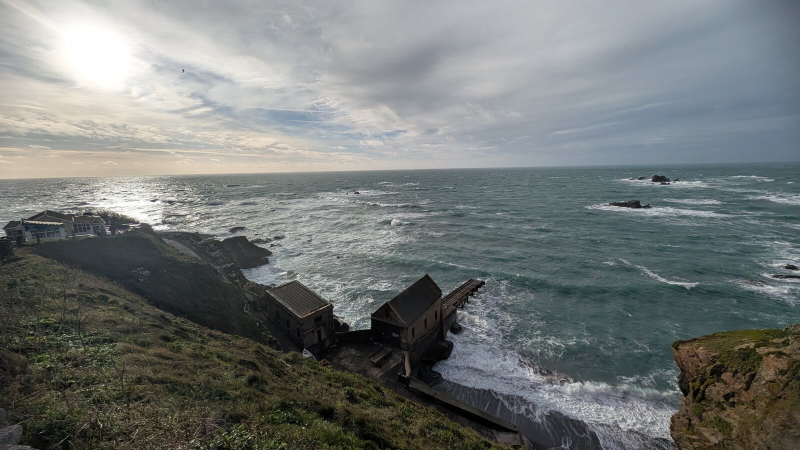 The Lizard Point lighthouse station and cafe perched on the cliffs at the southernmost tip of mainland Britain on a bright winter day, with the choppy Atlantic and offshore stacks beyond.
