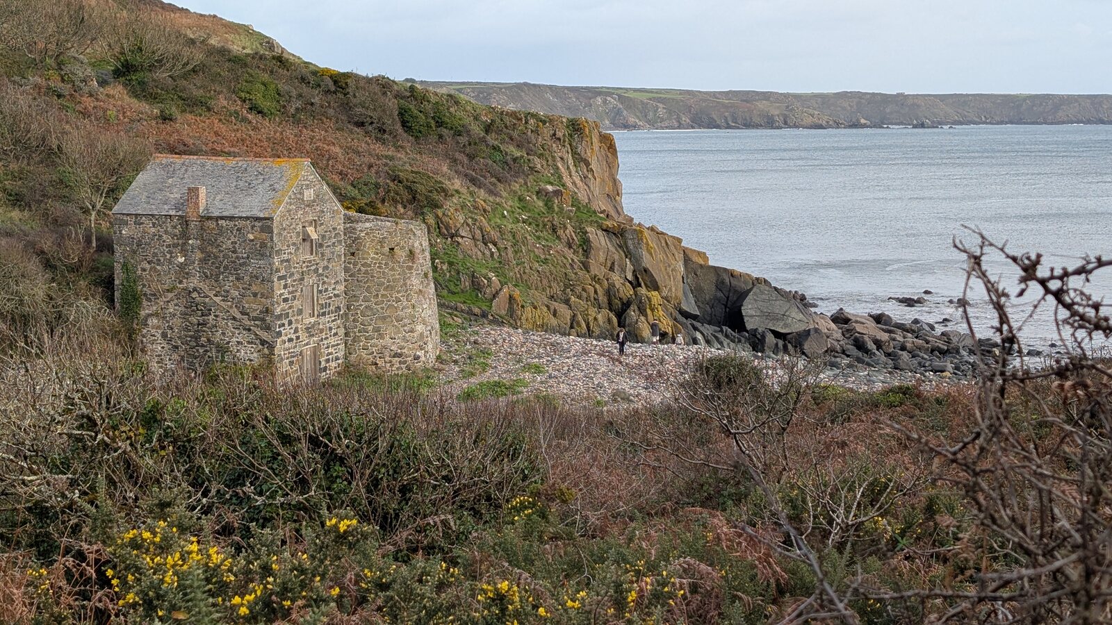 A stone-built former serpentine works on the south Cornish coast near Lizard Point, with a pebble beach and rocky coast beyond.