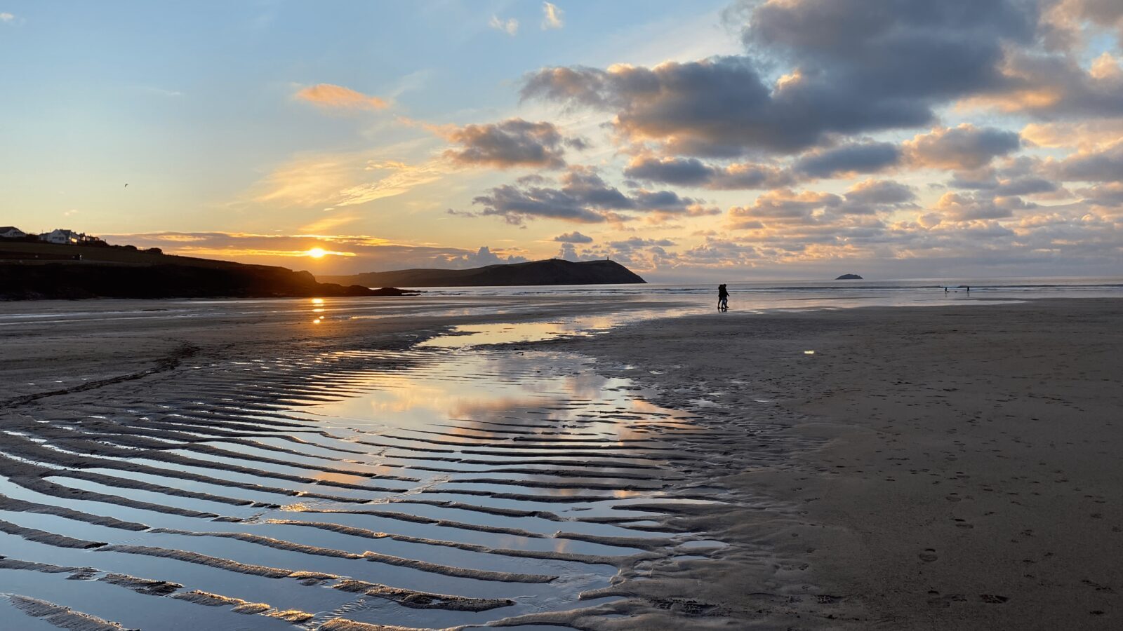 An empty Cornish beach in winter with clear skies and the low sun reflecting off pools of water left on the wet sand at low tide.