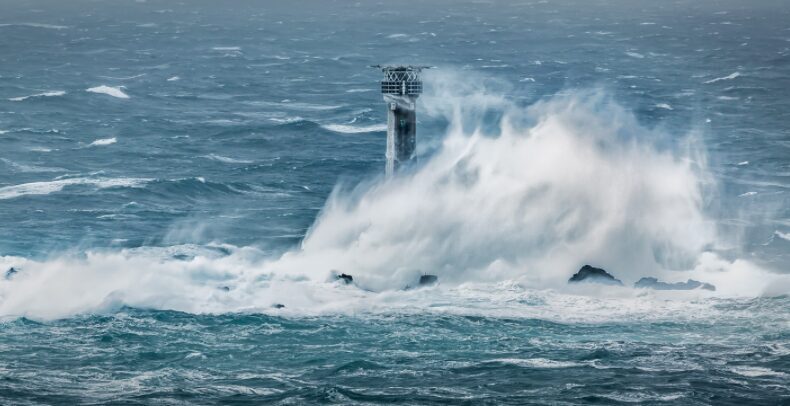 Longships Lighthouse on the rocks off Land's End being hit by a large white wave during a winter storm.