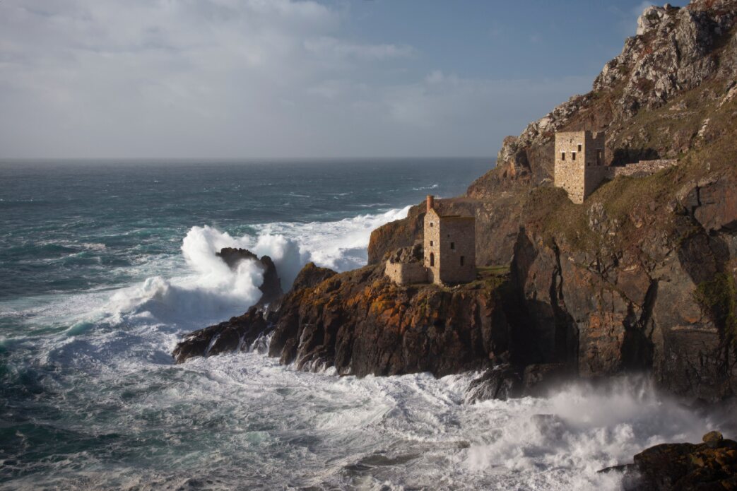 Storm waves hitting the rocks next to the old tin mines at Botallack in Cornwall, with the historic Crowns Engine Houses on the cliff edge above.