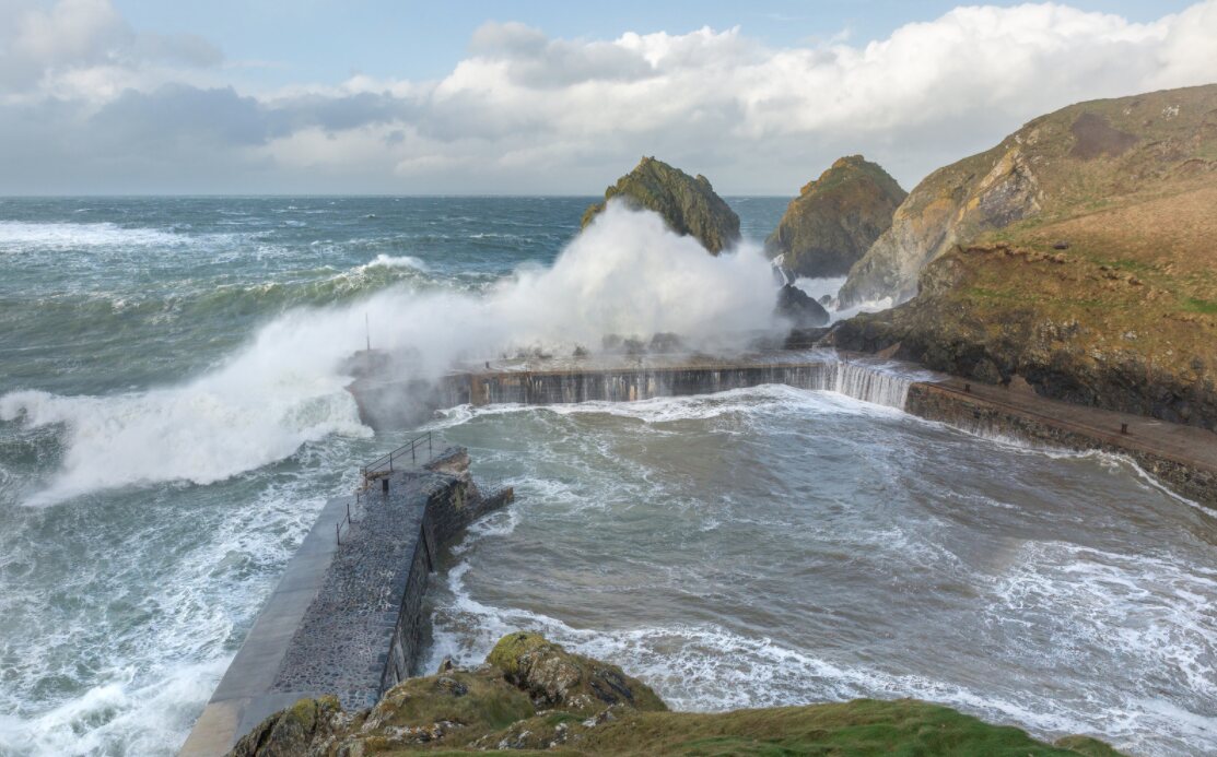 Huge storm waves crashing over the small harbour wall at Mullion Cove on the Lizard Peninsula in Cornwall.