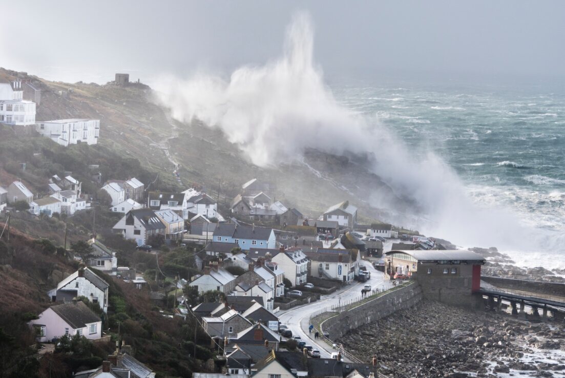Huge winter storm waves crashing over the headland at Sennen Cove in Cornwall, covering the village in sea spray.
