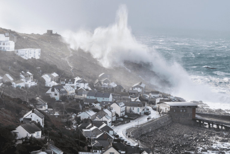Huge winter storm waves crash over the headland at sennen in cornwall, covering the village in sea spray