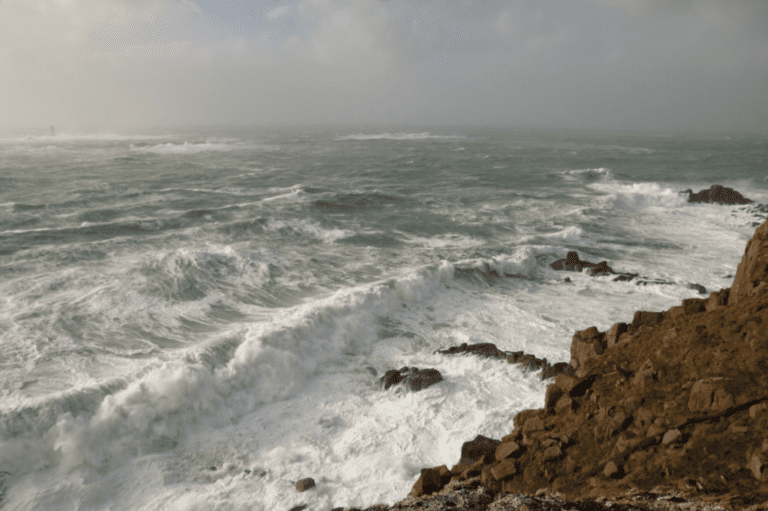 Large waves hit the coast at land's end cornwall during a storm. Longships lighthouse can be seen in the background