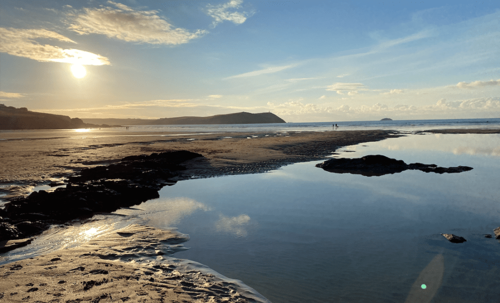 An empty beach in winter in cornwall with clear blue skies reflecting into a pool on the beach